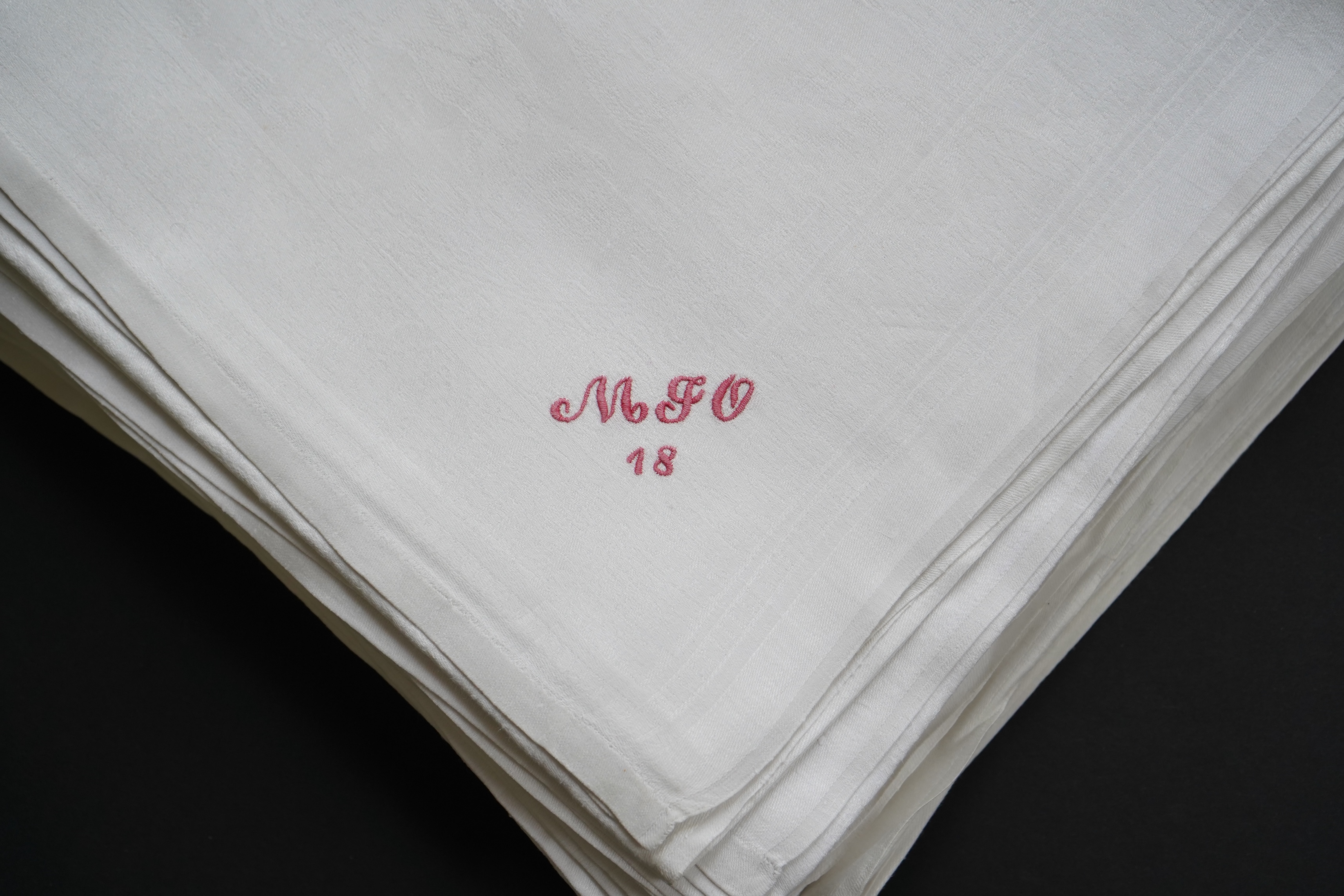 A set of nine red monogrammed 19th century large damask dinner napkins and a similar set of coarser French provincial damask napkins, the large set, decoratively designed with a boating river scene, amongst classical bui